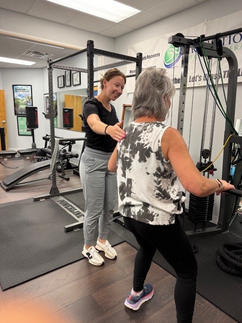 Older person doing strength training with a trainer supporting