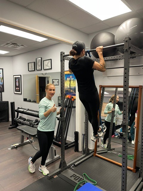 Image show a person doing pull-ups with a trainer present.
